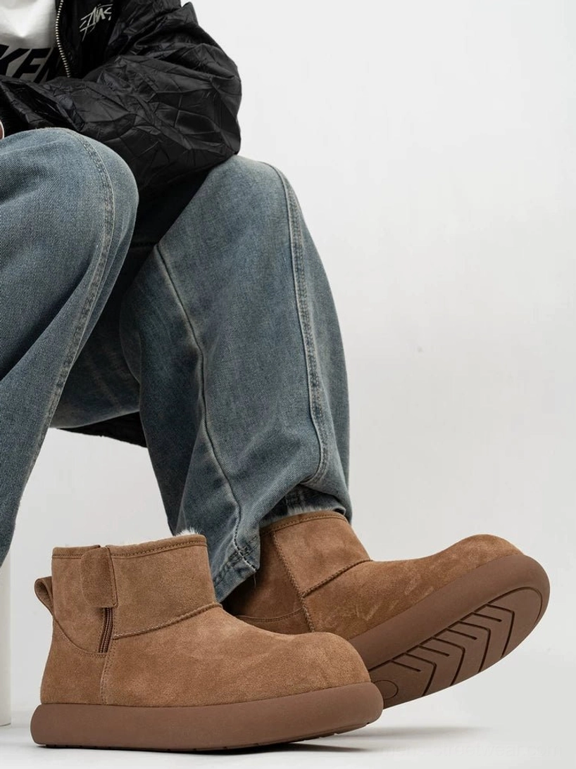 Chestnut brown men's shearling ankle boots worn with blue jeans and a black jacket, highlighting the rounded toe, suede upper, thick rubber sole, and side strap detail