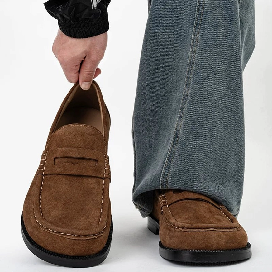 Close-up of chestnut suede penny loafers worn with baggy denim, highlighting the penny strap, visible suede nap, square toe, and smooth shoe interior