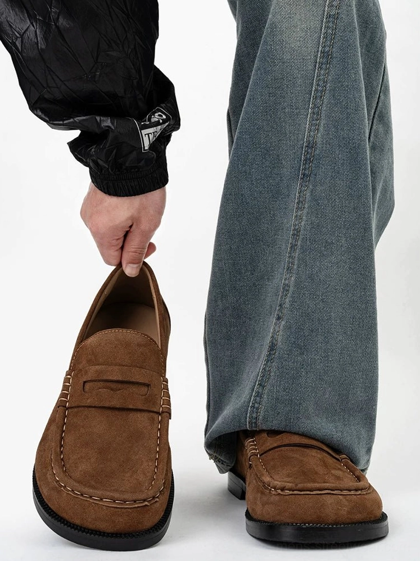 Chestnut suede penny loafers styled with loose blue jeans, featuring the rounded square toe, stitched vamp, and black rubber outsole