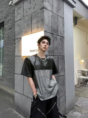 Front three-quarter view of a two-tone chrome grid patchwork techwear T-shirt with black crocodile-effect upper panels and silver textured torso, styled with black cargo pants and layered necklaces