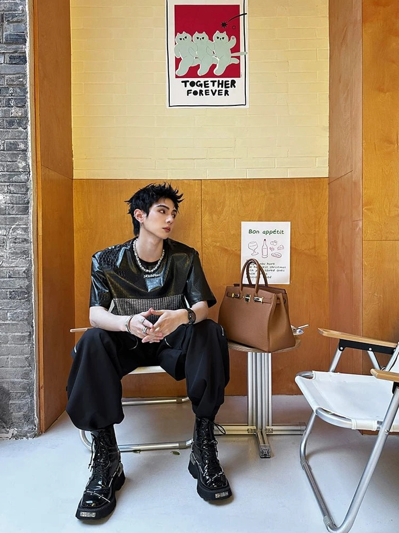 Seated front view of the black and silver chrome grid patchwork techwear T-shirt styled with layered jewelry, black cargo pants, and combat boots