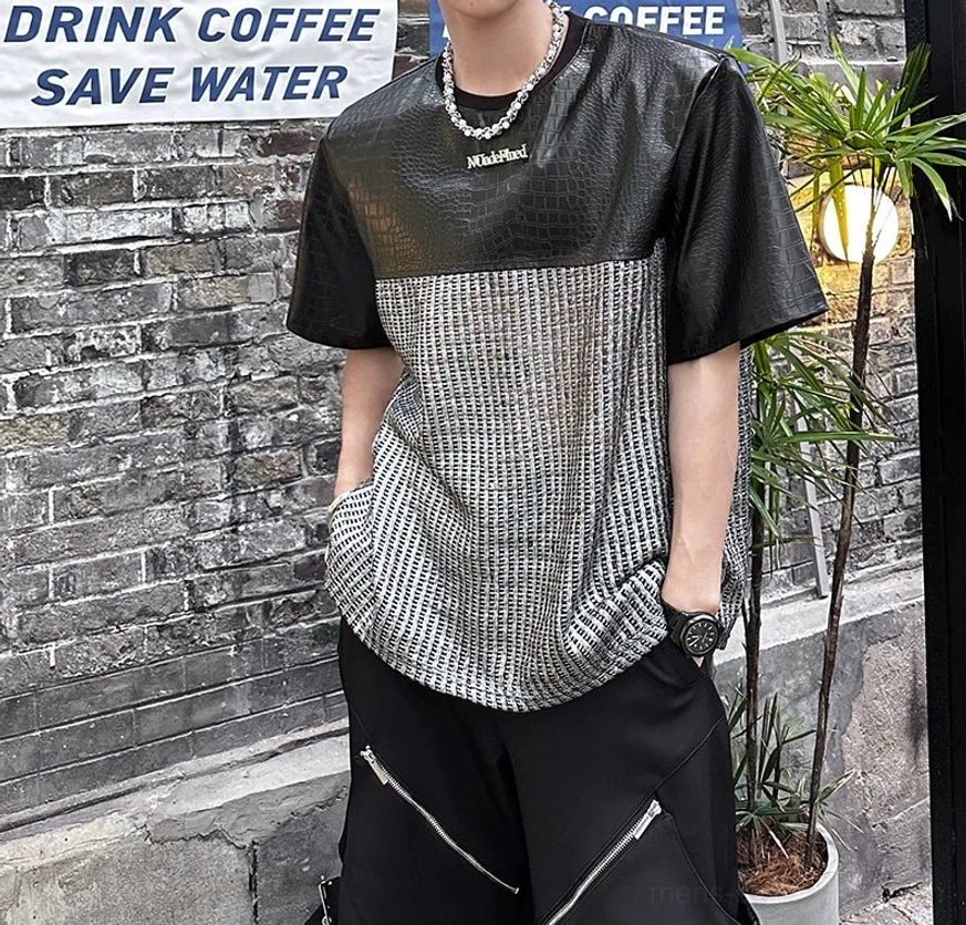 Close-up front three-quarter view of the chrome grid patchwork techwear T-shirt showing black crocodile-effect texture, silver woven body, chest detail, and layered necklace