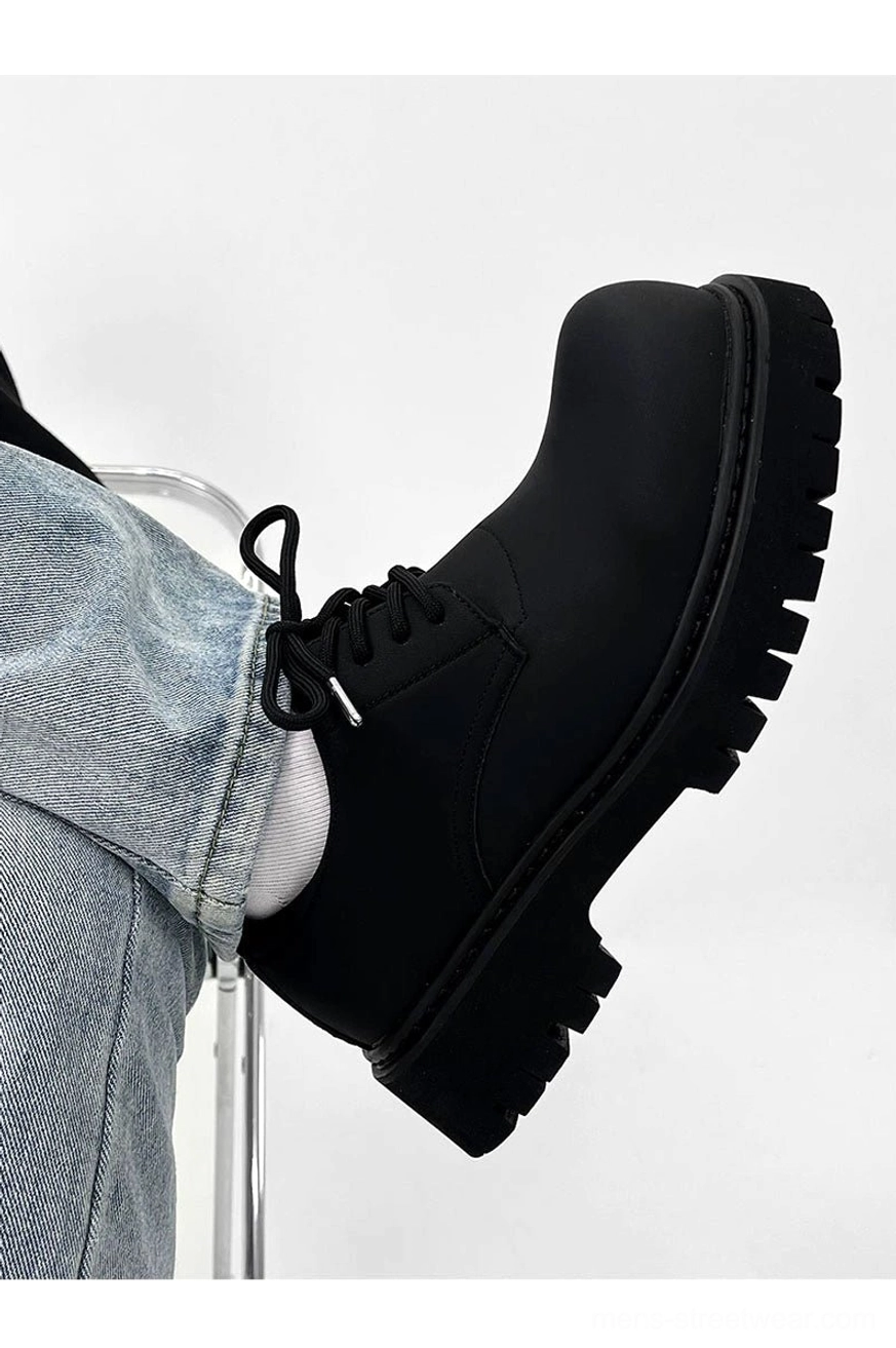 Side view of a chunky black matte derby shoe worn with jeans showing metallic lace aglets and anti-slip sole tread
