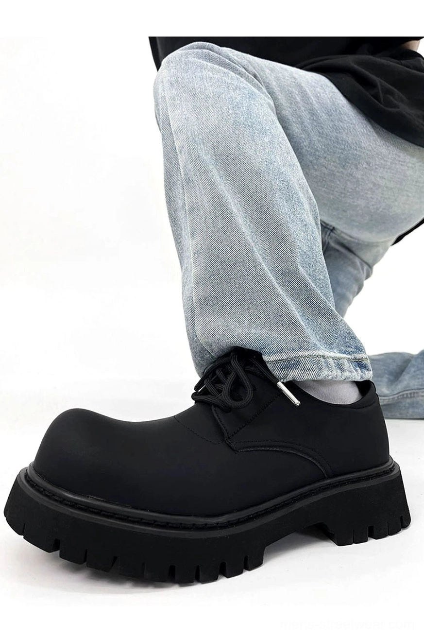 Front three-quarter view of a chunky black matte platform derby shoe worn with light blue jeans and a black top