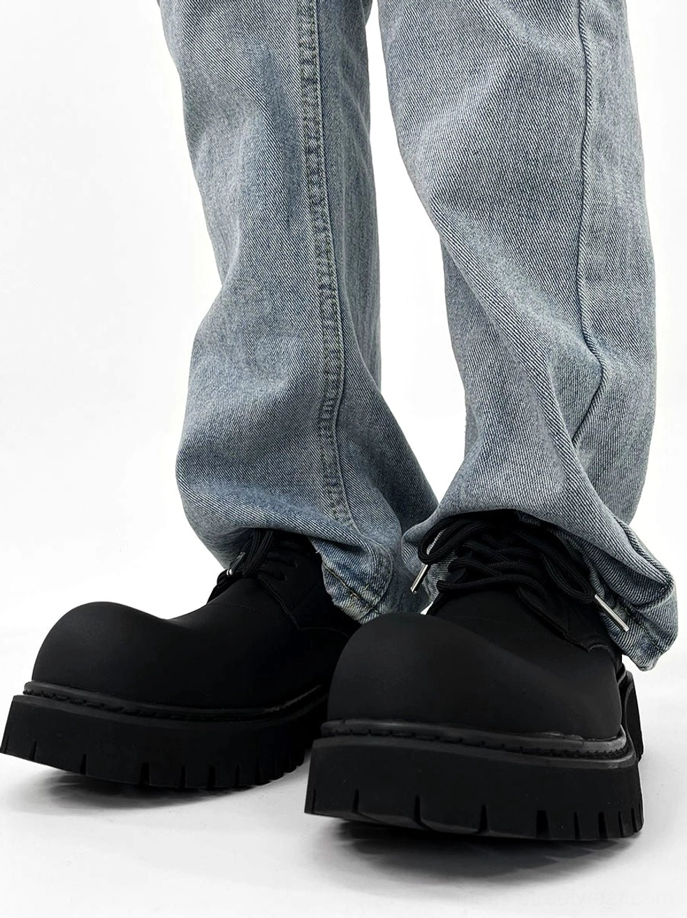 Pair of chunky black platform derby shoes worn with cuffed light blue jeans showing deep anti-slip lug tread