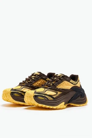Yellow and dark brown chunky dad sneakers with jagged layered panels and a rugged thick outsole displayed on a white studio background