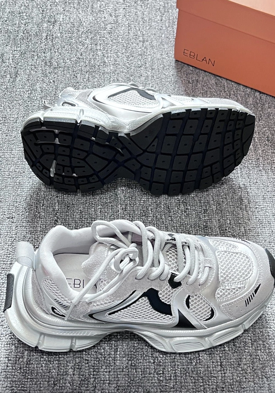 Chunky metallic mesh runner sneakers showing breathable upper and rugged black sculpted outsole on a gray carpet