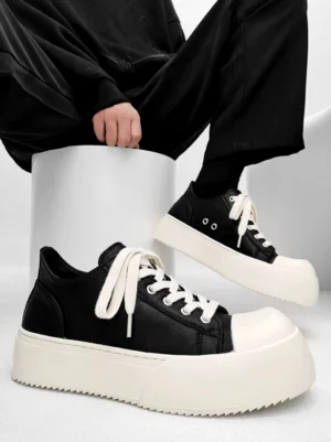 Black and off-white chunky platform low-top sneakers shown in side view with a male model wearing black pants, matte leather upper, rounded rubber toe cap, and serrated thick sole