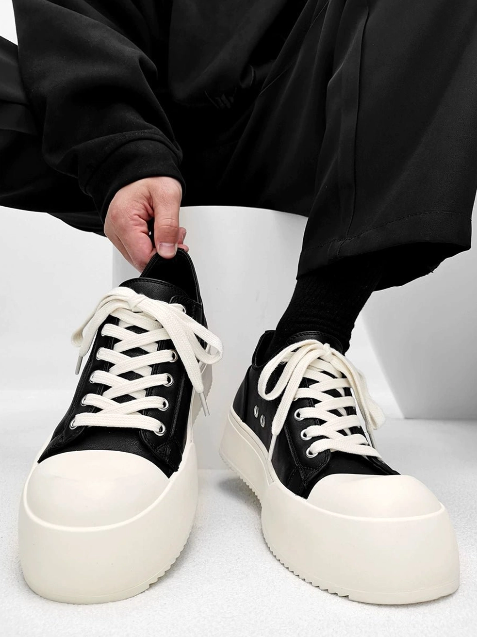 Chunky platform low-top streetwear sneakers shown from the front on foot with flat laces, visible tongue, rounded toe cap, and thick off-white platform sole