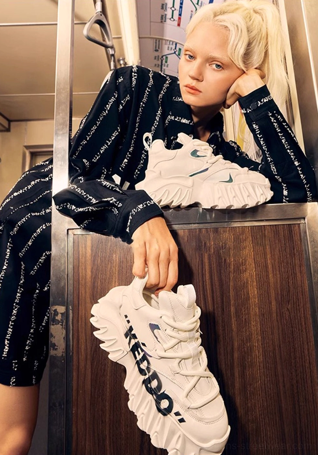 Close-up of chunky platform sneakers styled with printed loungewear near a subway handrail, highlighting thick white soles and graphic streetwear detailing