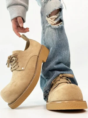 Khaki suede platform derby shoes shown from an angled side view with a chunky crepe rubber sole and ripped flared jeans