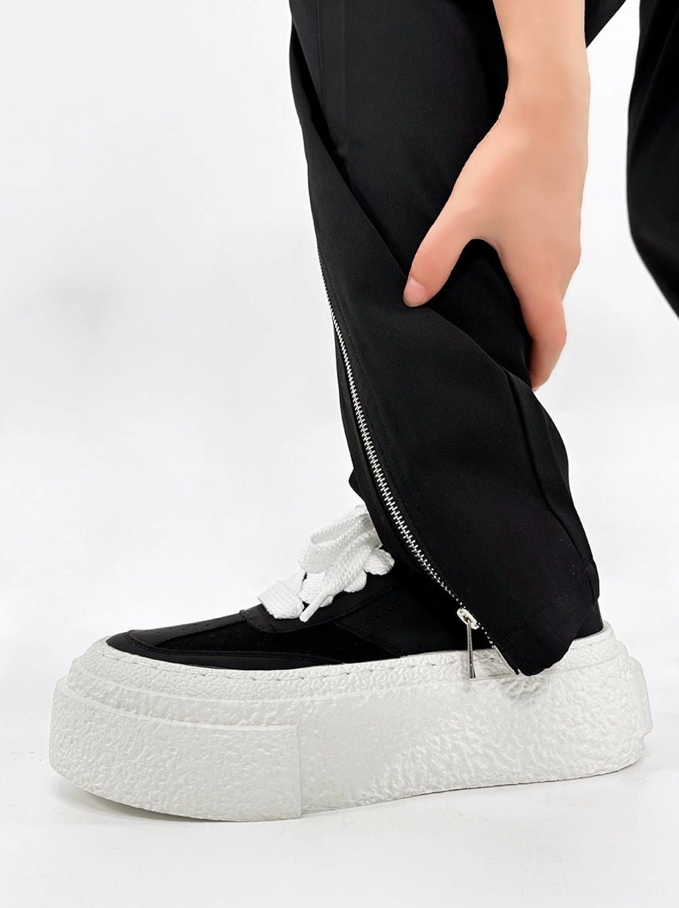 Black chunky textured sole sneakers with white platform rubber soles worn with black zippered streetwear trousers