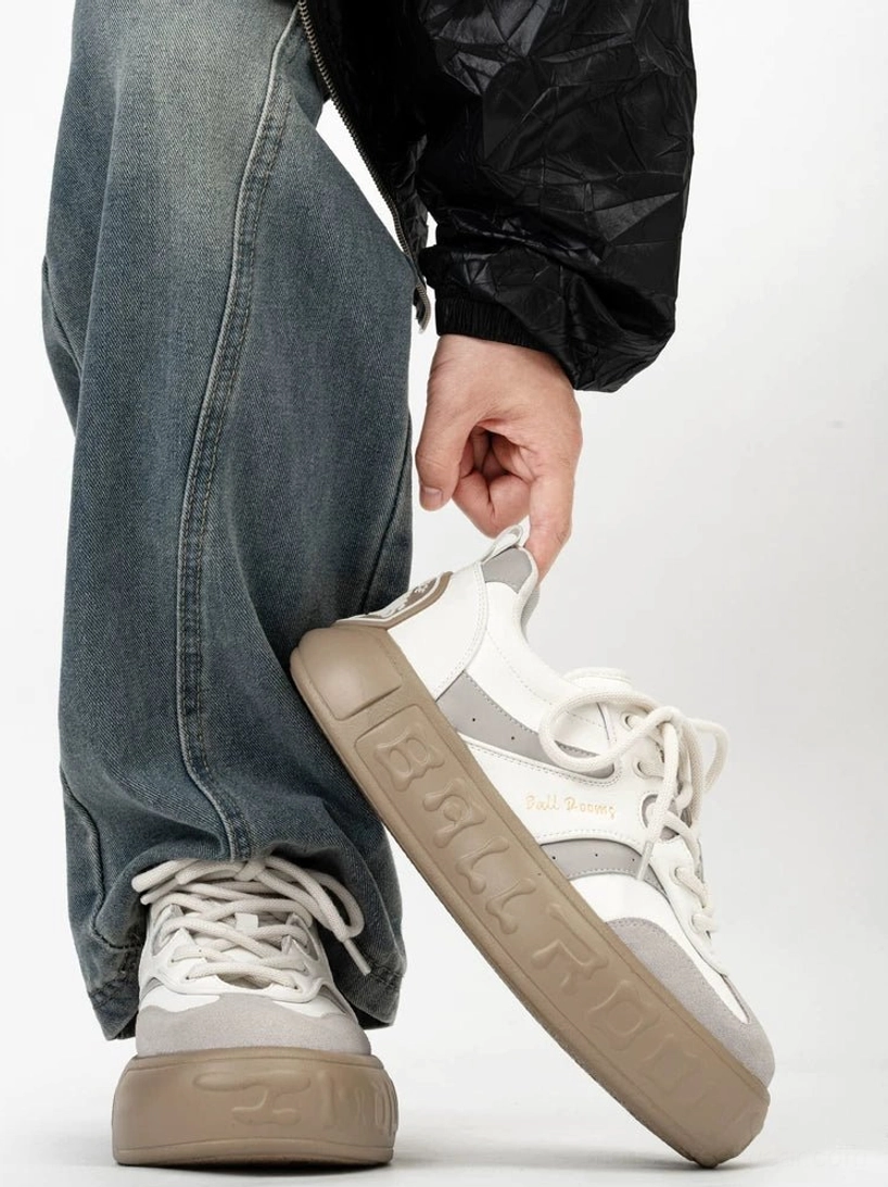Chunky white gray and brown color block platform sneakers shown from a low rear three quarter angle with baggy jeans and a black streetwear jacket