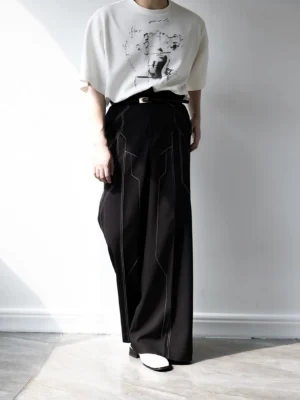 Front three-quarter view of black circuit trace wide leg trousers with architectural contrast stitching, high waist, tailored silhouette, graphic streetwear tee, and white flat shoes