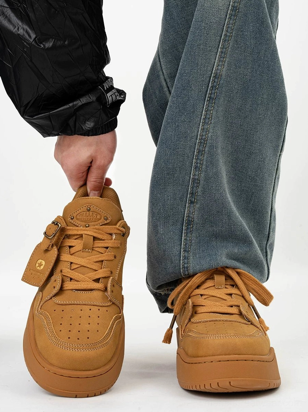 Wheat suede-style platform skate sneakers shown from the front with one shoe held and a pair worn with baggy blue jeans and a black streetwear windbreaker