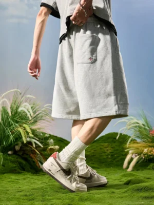 Heather ash cloud fleece drawstring lounge shorts shown from a rear three quarter angle on a model wearing a cropped tee crew socks and retro sneakers in an outdoor streetwear setting