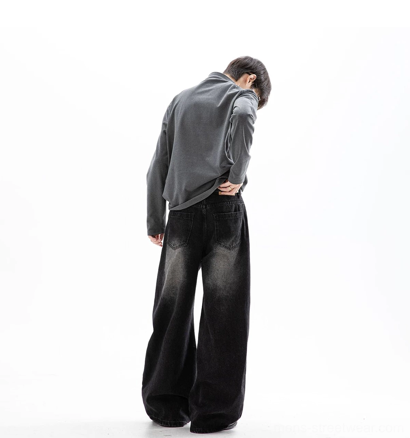 Washed black Korean streetwear ultra wide leg jeans shown from the back in a minimalist studio