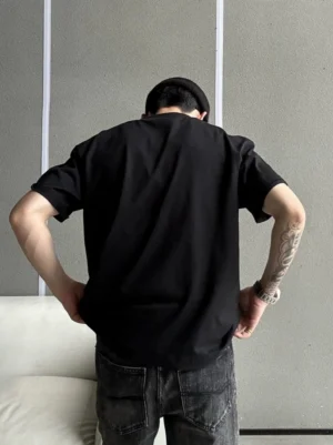 Back view of a relaxed black boxy crew neck streetwear T-shirt worn by a male model in a minimalist studio