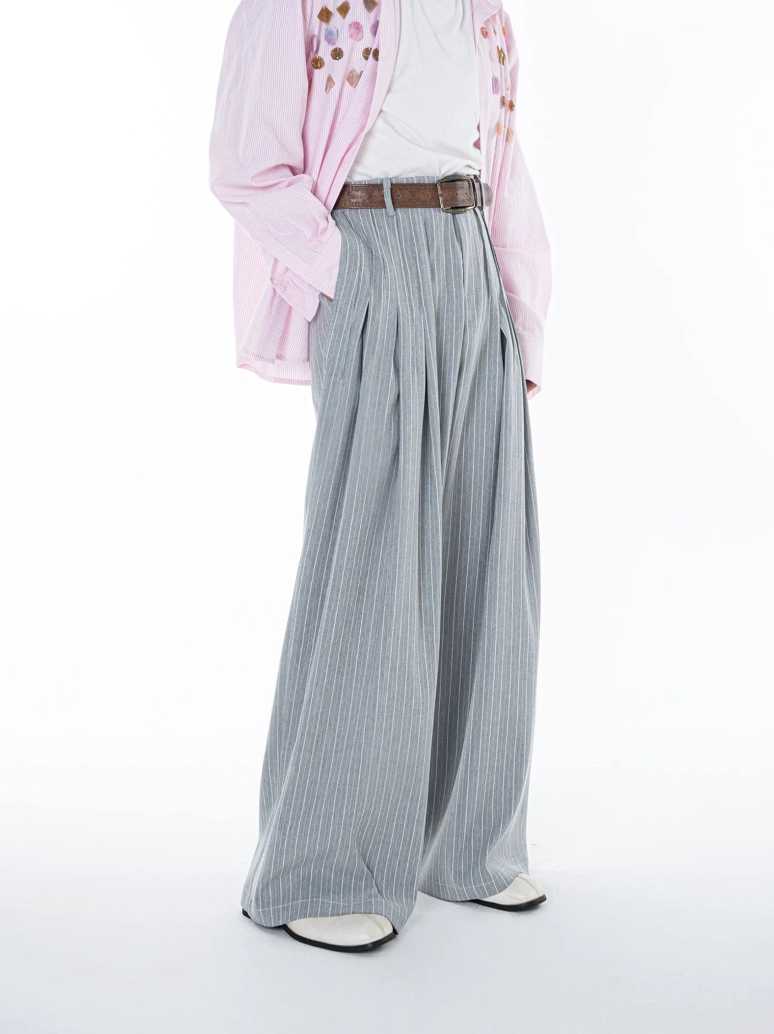 Cloudline grey pinstripe pleated ultra wide leg trousers shown from the front with a pink embroidered shirt and white leather shoes
