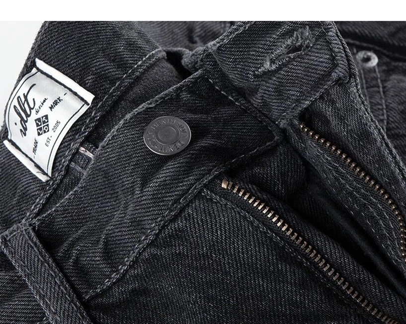 Overhead close-up of washed black denim jeans waistband, metal zipper fly, button closure, and interior size label