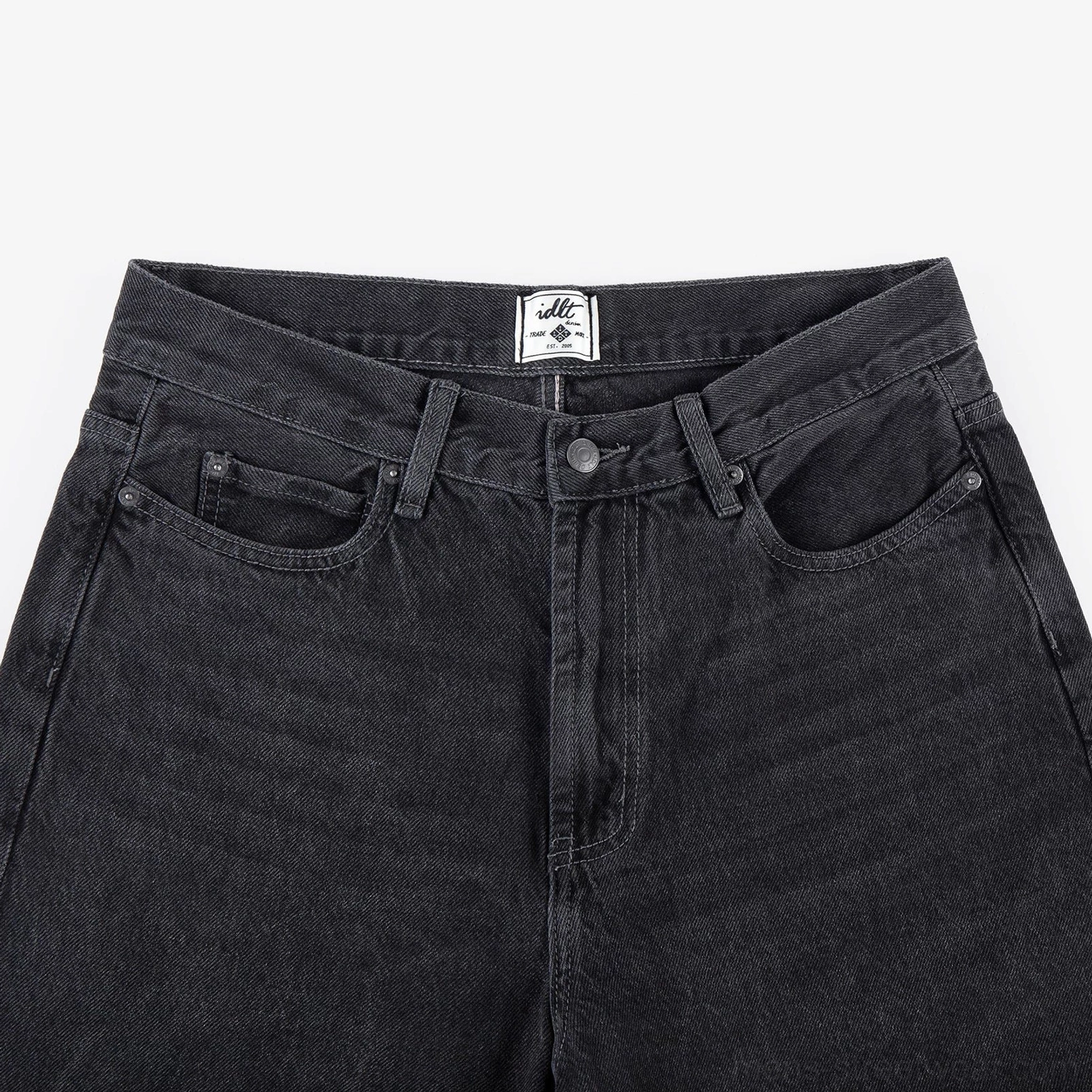 Close-up of washed black wide-leg jeans high-rise waist, front pockets, button fly, and textured cotton twill denim
