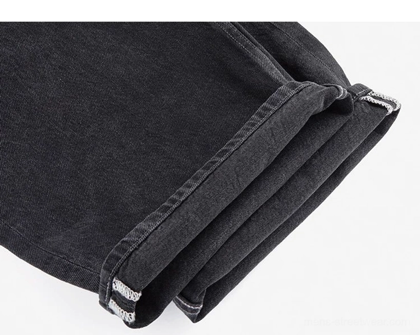 Close-up of washed black wide-leg denim trouser hem showing twill weave, structured leg opening, and folded hem finish