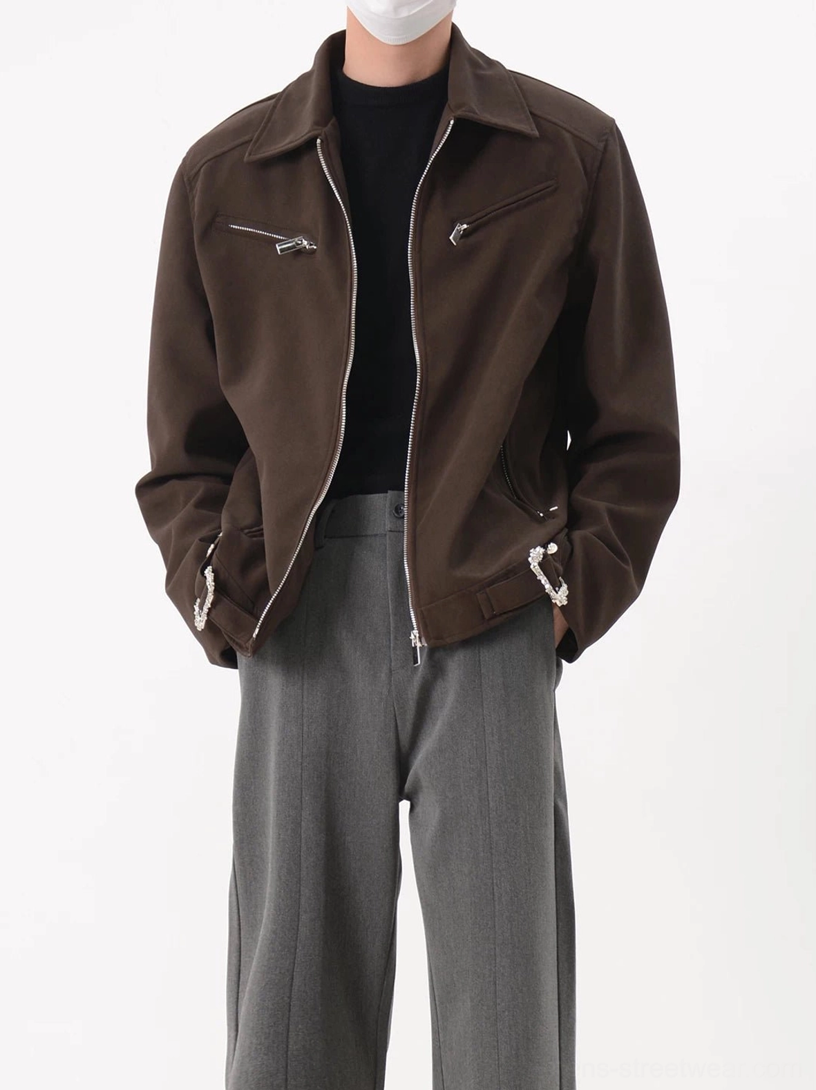 Dark coffee brown cropped zip-up moto jacket with pointed collar silver zippers and structured streetwear fit styled with grey wide-leg trousers