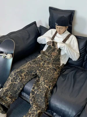 Coffee brown leopard print baggy skate overalls worn with a white turtleneck and black cap while sitting on a black leather sofa