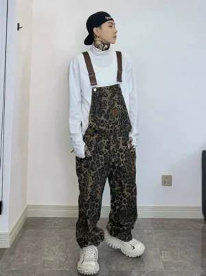 Front full-body view of coffee brown leopard print cotton skate overalls with adjustable straps, bib pocket, and chunky white sneakers