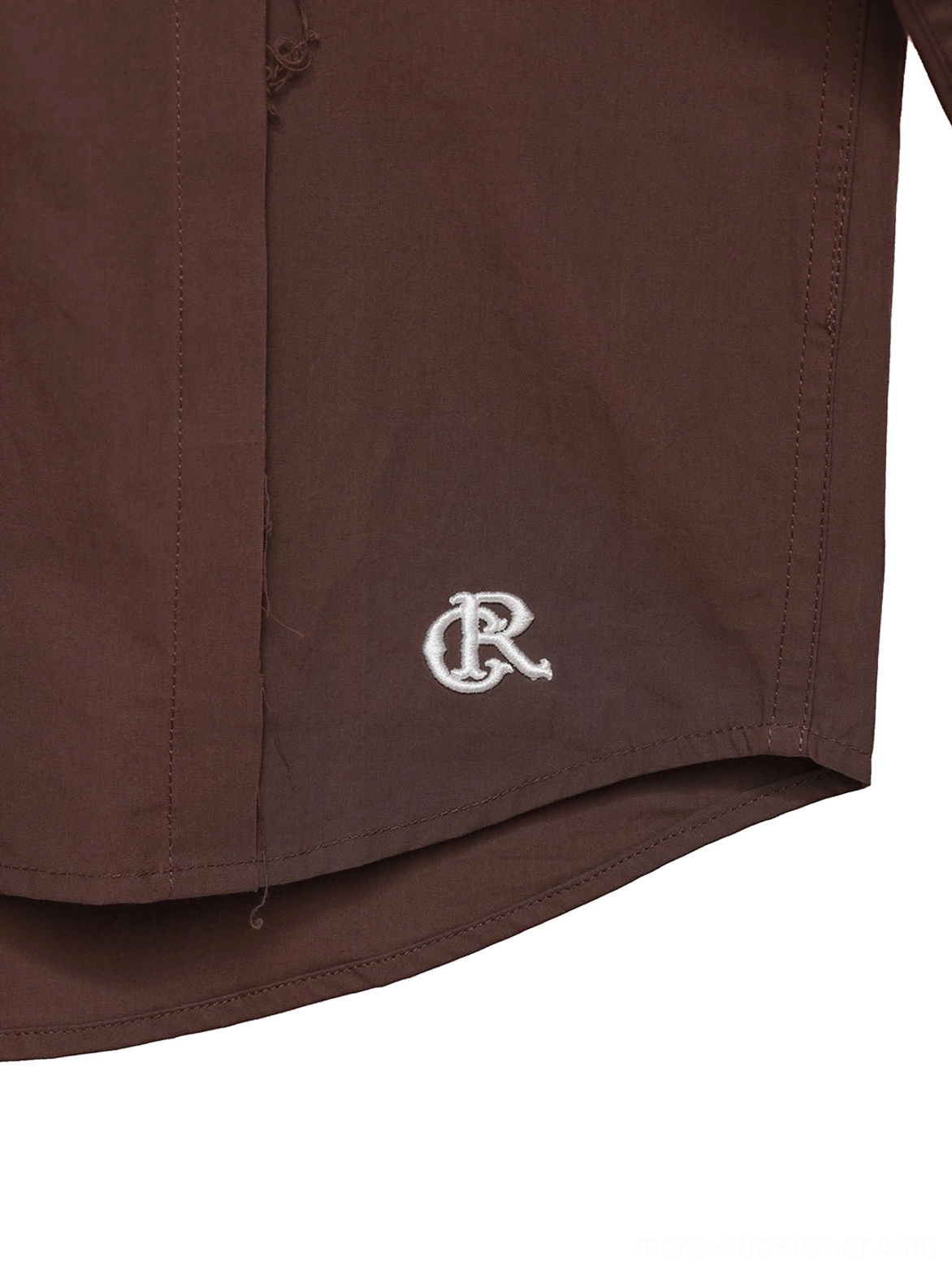 Close-up of curved hem and subtle white embroidered detail on coffee brown cotton poplin overshirt
