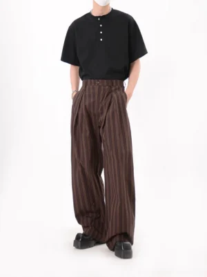 Coffee brown vertical striped pleated trousers styled with a black henley shirt and leather shoes in a minimalist studio