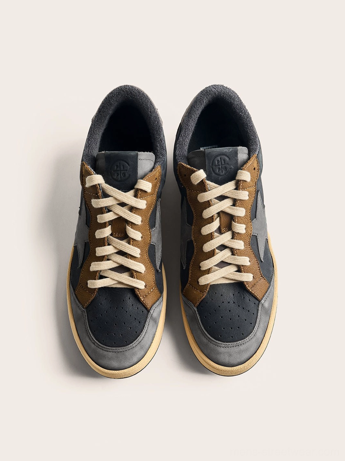 Top-down flat lay of a pair of coffee and gray star panel retro low-top sneakers with complete lacing and off-white rubber outsoles