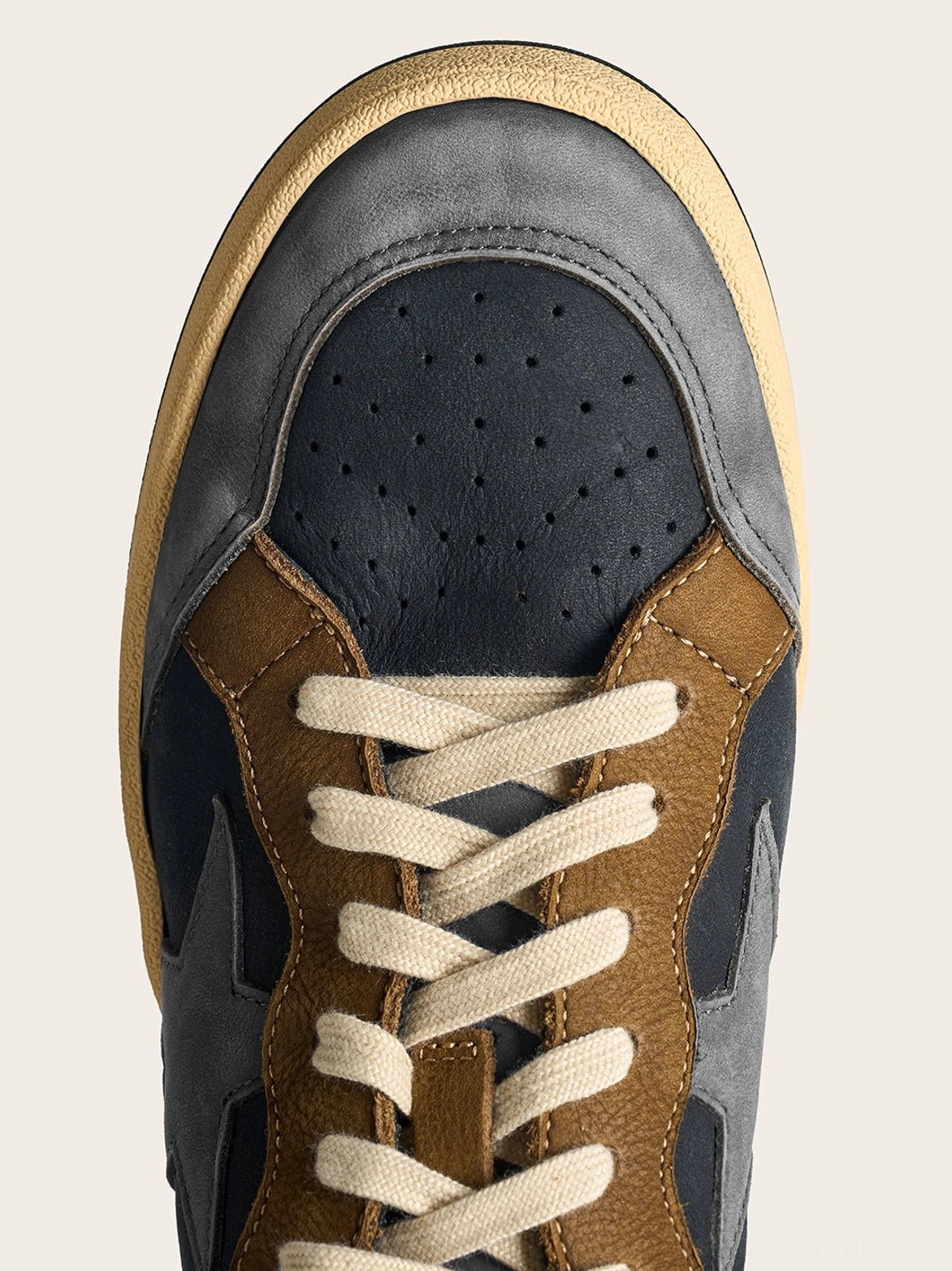 Extreme close-up of the retro star panel sneaker toe box showing perforated leather, flat beige laces, and layered color-blocked materials