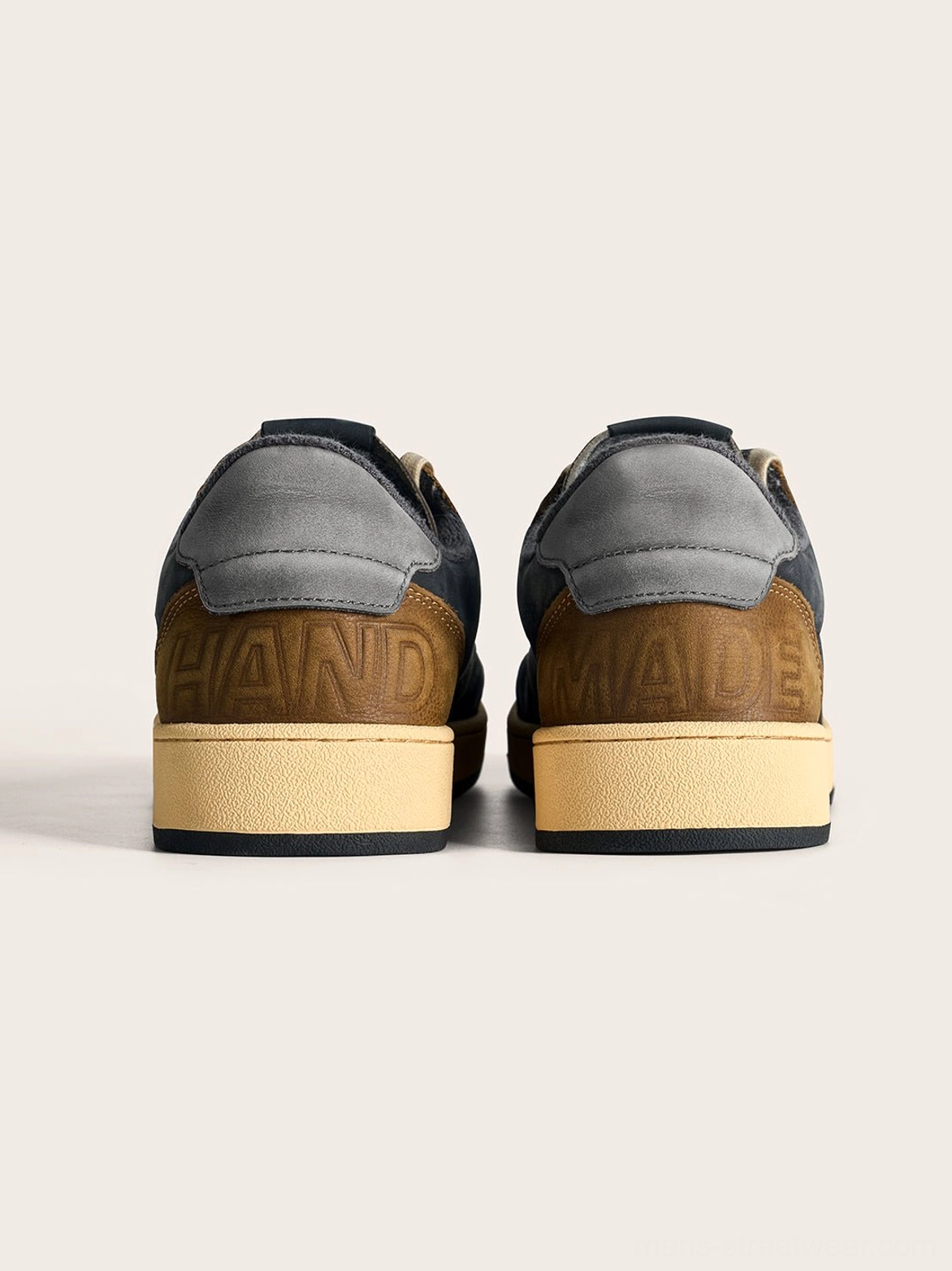 Rear view of coffee and gray retro low-top sneakers showing the contrast heel panels, embossed handmade detail, and aged rubber outsole