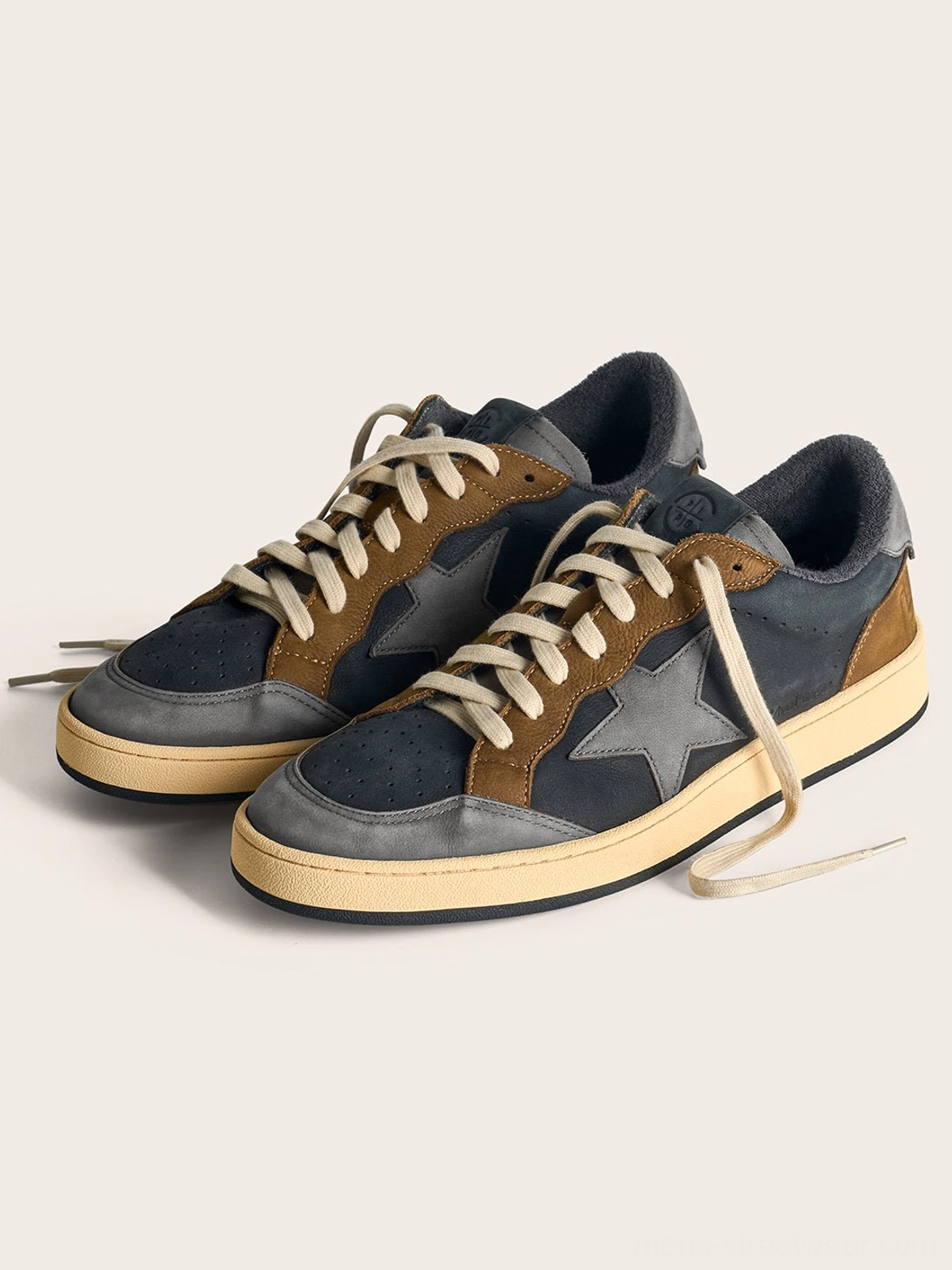 Three-quarter view of coffee and gray retro low-top sneakers displaying the oversized side star, layered upper, and vintage off-white sole