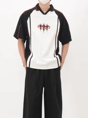 Model wearing a color block polo soccer jersey with black shoulder panels, white torso, red trim, and loose streetwear trousers