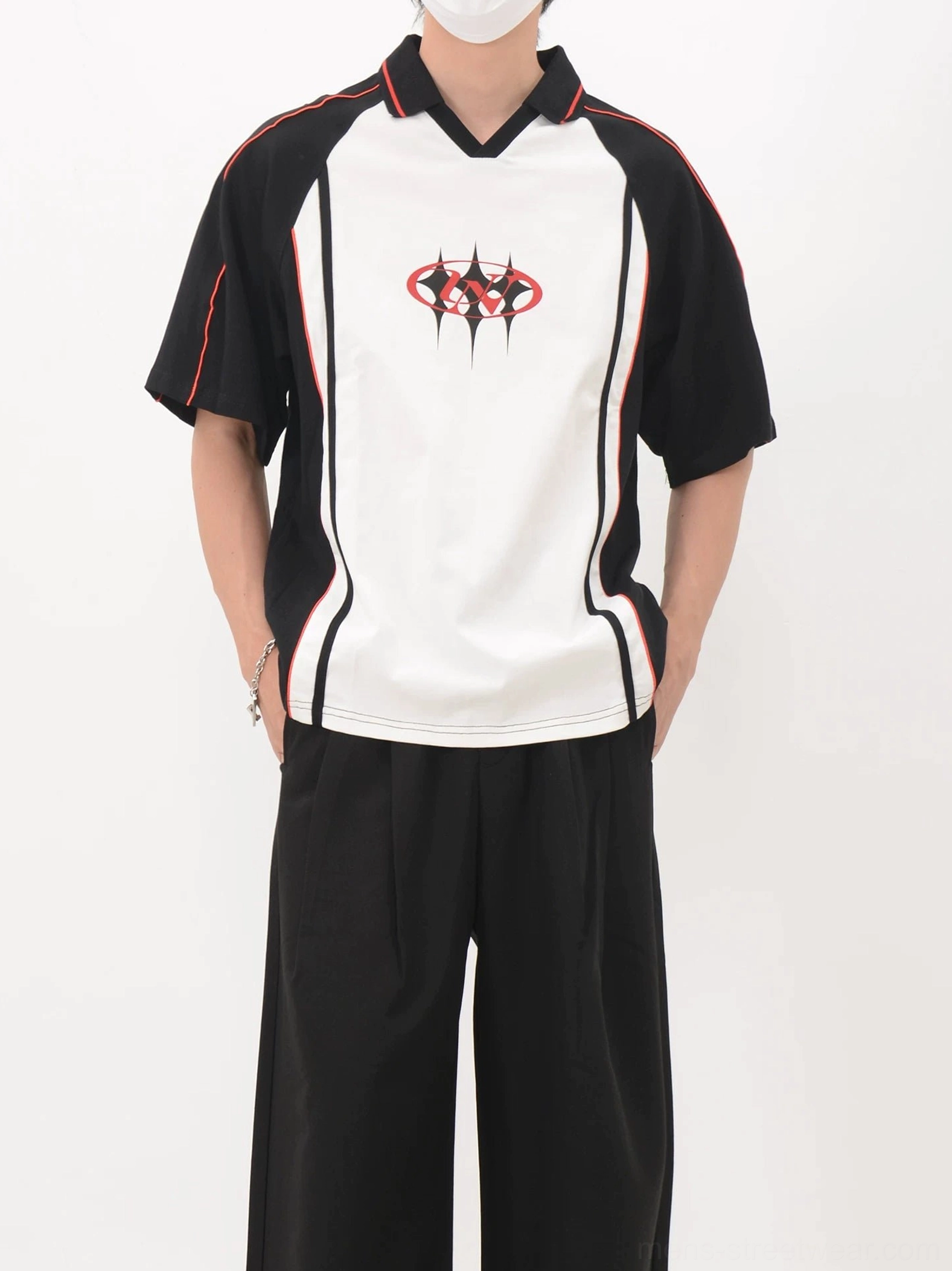 Model wearing a color block polo soccer jersey with black shoulder panels, white torso, red trim, and loose streetwear trousers