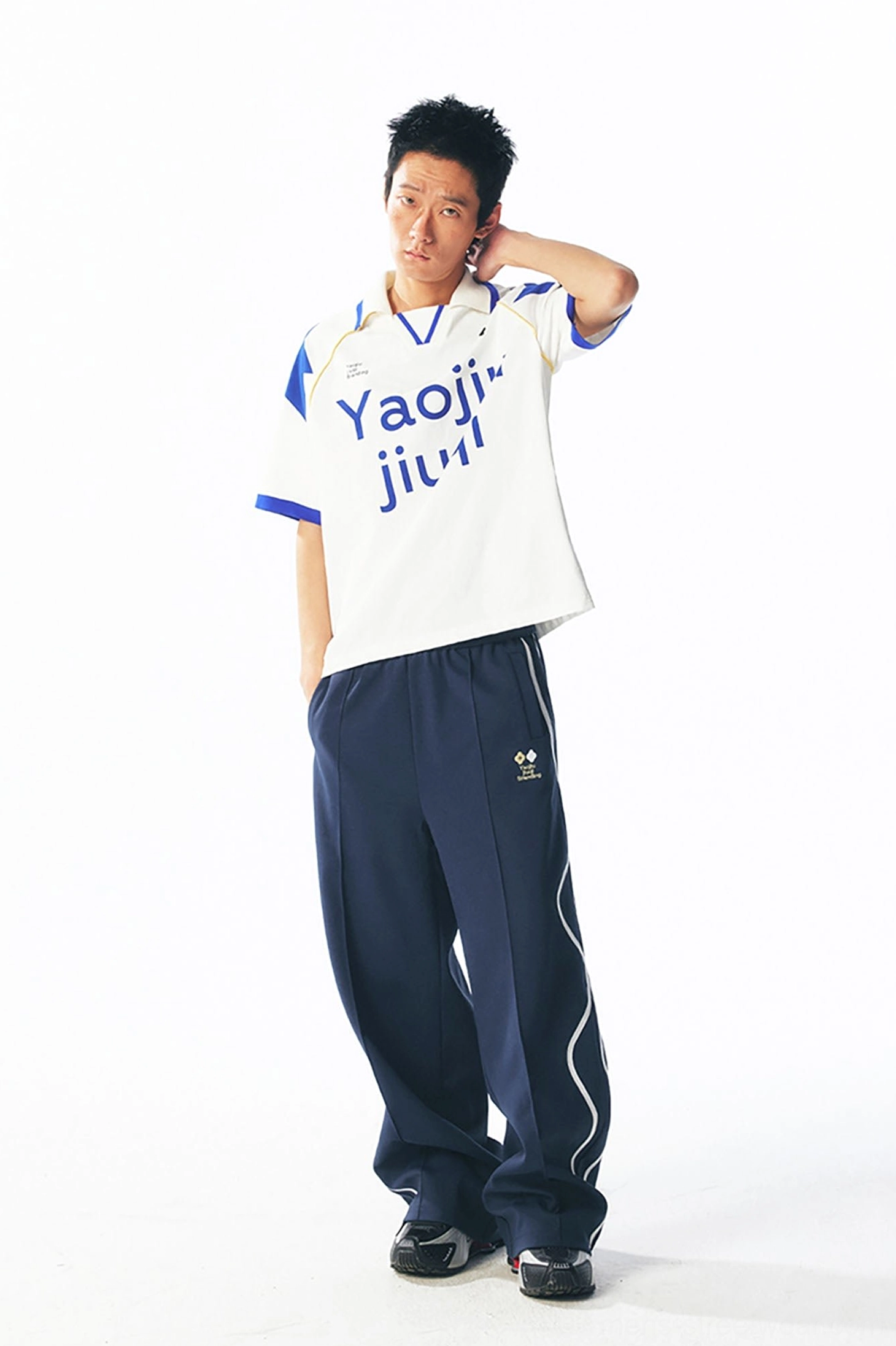 Side view of a color-block retro football jersey with Yaojiu jiuqi print styled with navy sport pants and white side stripes