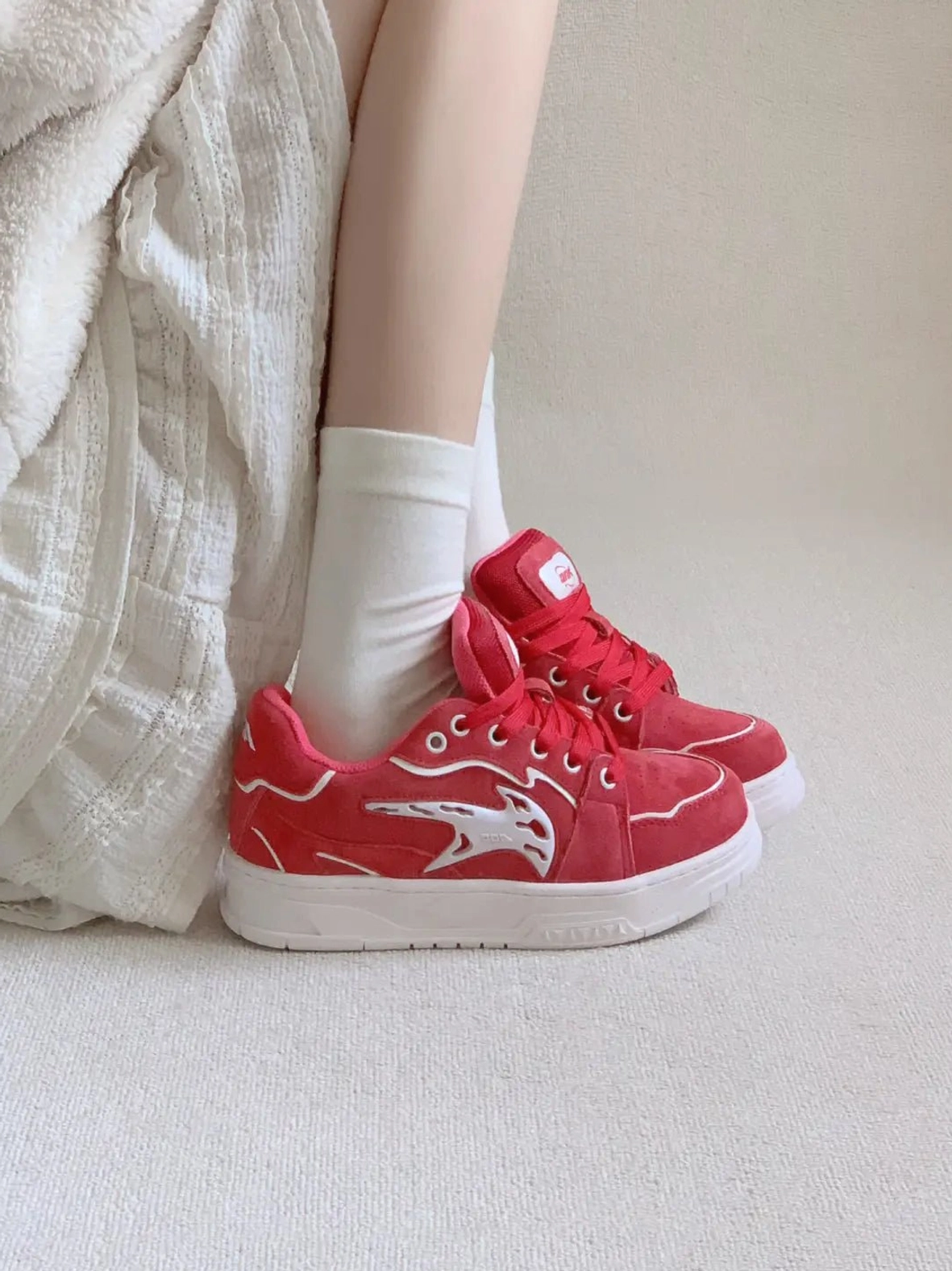 Red low-top skate sneakers worn with white socks in an overhead lifestyle view, showing textured red uppers and chunky white rubber soles