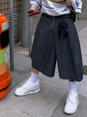 White basketball-inspired court sneakers styled with wide black shorts, striped tee, and crew socks in an urban streetwear outfit