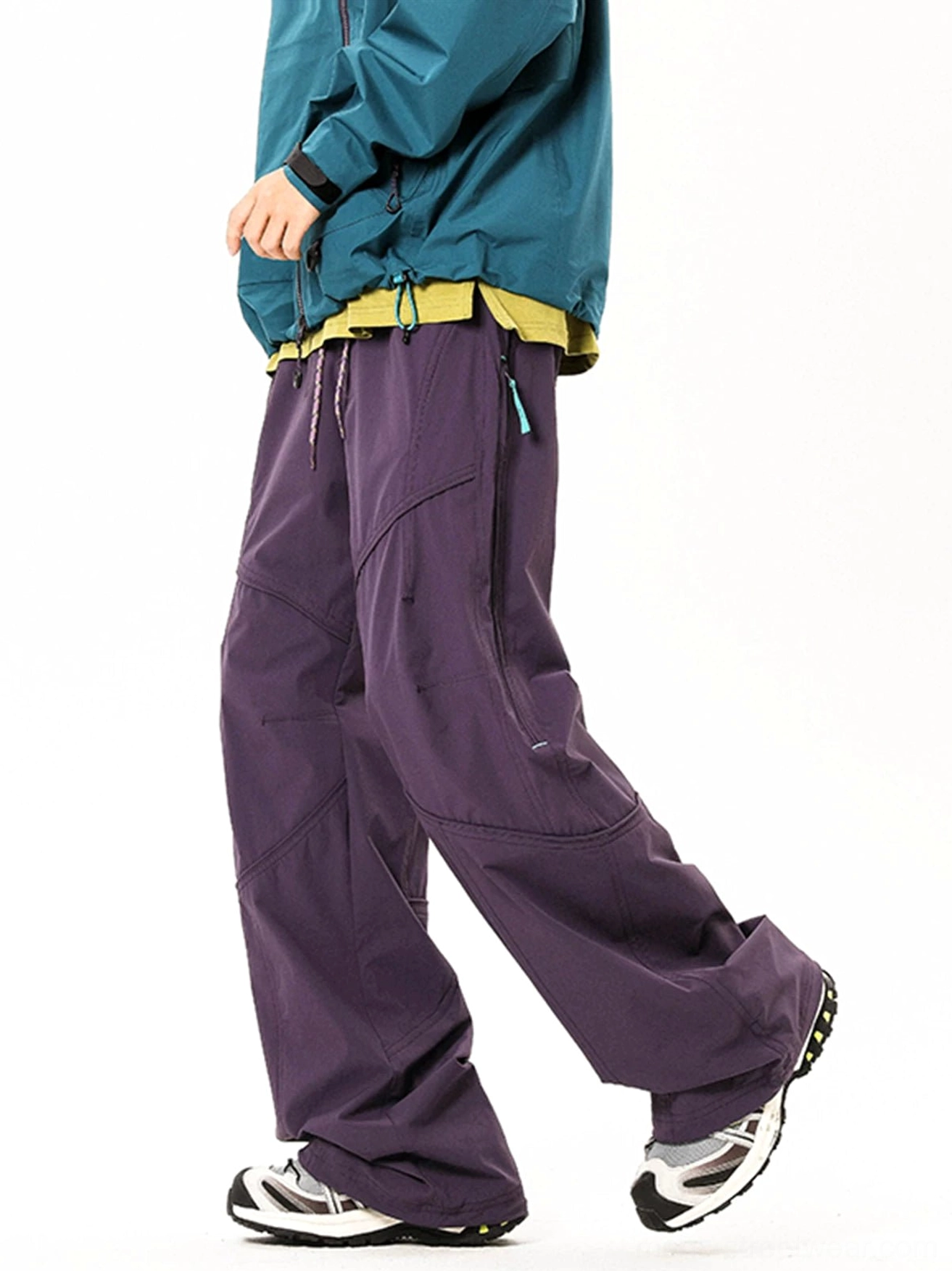 Dark purple wide-leg tech cargo pants shown in a walking side view with curved panel seams and outdoor jacket