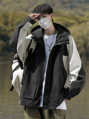 Male model wearing a black and off-white colorblock techwear windbreaker jacket with hood and cargo pockets outdoors