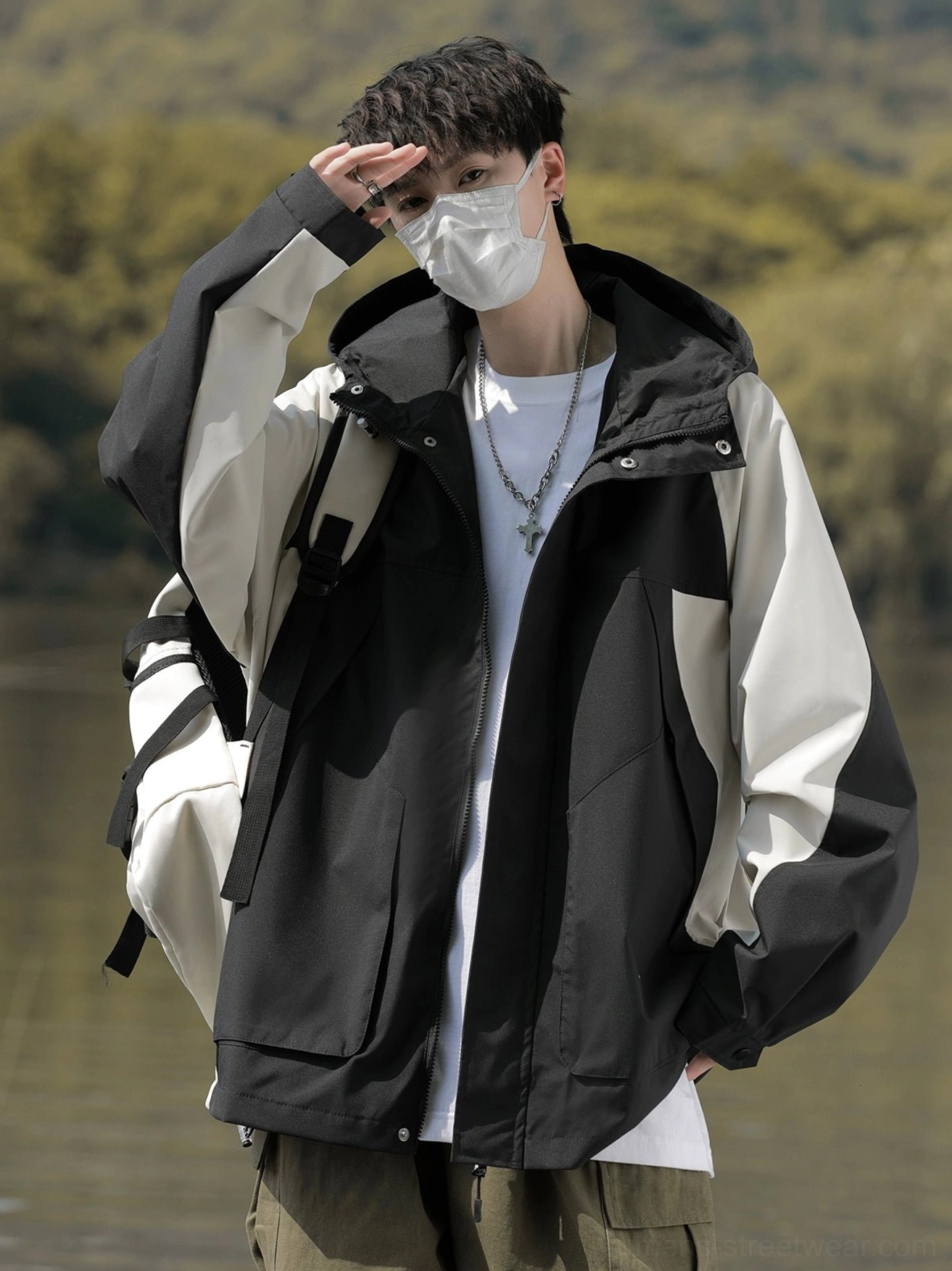 Male model wearing a black and off-white colorblock techwear windbreaker jacket with hood and cargo pockets outdoors
