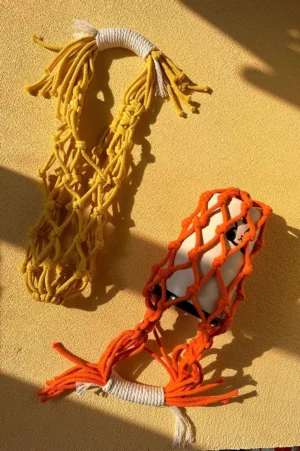 Yellow and orange macrame water bottle carriers with knotted cotton net holders and tassel handles