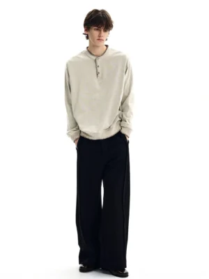 Off-white contrast stitch Henley sweatshirt on male model with black wide-leg pants in minimalist studio