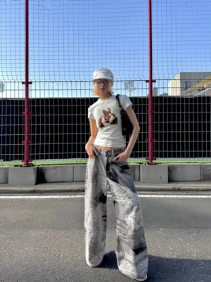 Washed gray convertible flying bird graphic wide-leg jeans worn in an outdoor streetwear outfit, showing the artistic portrait and damask print from a three-quarter front view