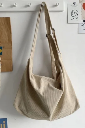 Light khaki corduroy slouchy crossbody bag with ribbed texture and adjustable shoulder strap hanging on wall hook