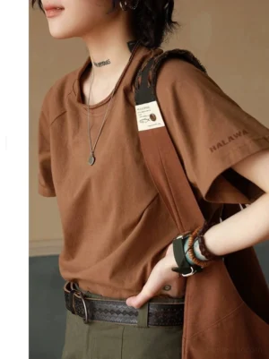 Brown cotton raglan sleeve T-shirt styled with layered necklaces, bracelets, leather belt, and canvas shoulder bag