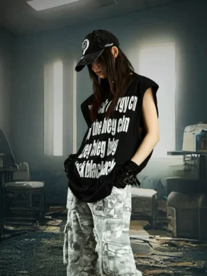 Black cracked text oversized sleeveless streetwear muscle tee front view styled with camouflage cargo pants in a dark industrial setting