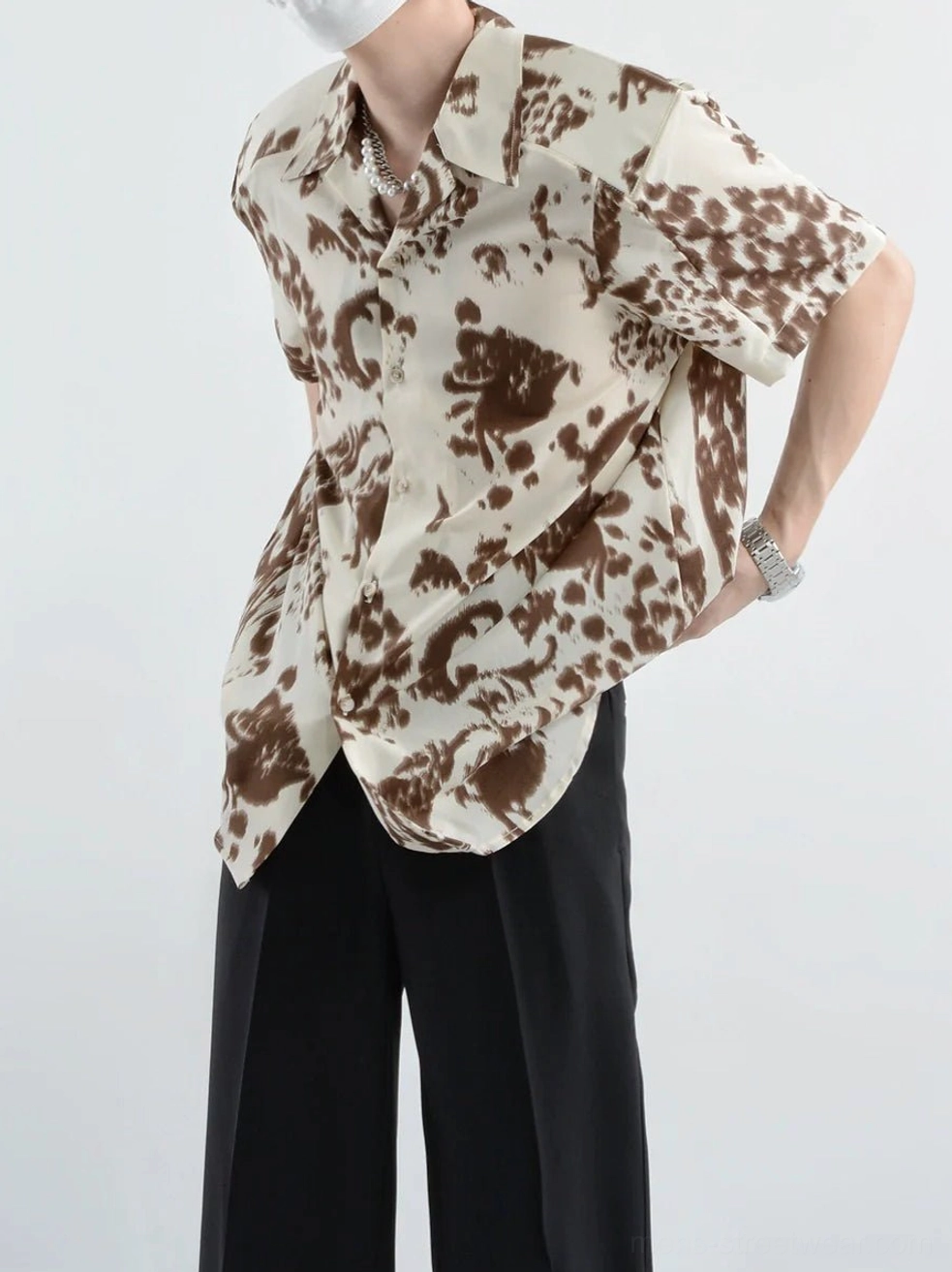 Three-quarter side view of a model wearing a cream and brown abstract paisley print short-sleeve shirt with relaxed fit and wristwatch
